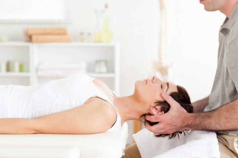 Chiropractor adjusting a woman's neck while she lies on her back.