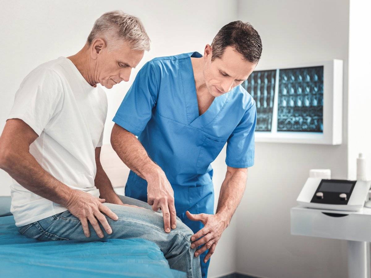 Chiropractor examining the knee of an older male patient in a clinic.