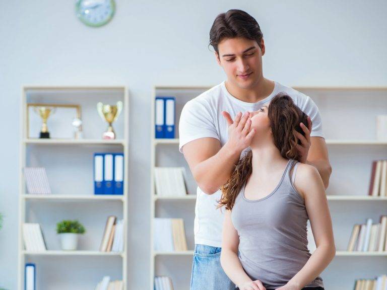 Chiropractor performing a neck adjustment on a female patient in a clinic with bookshelves and trophies.