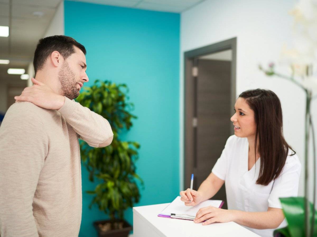 Man with neck pain talking to a clinic receptionist.