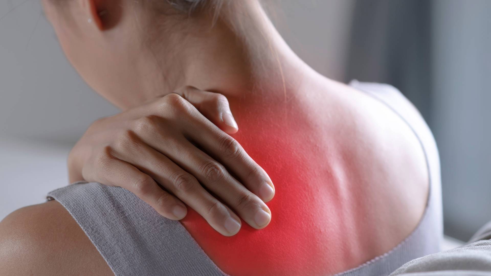 Person touching their shoulder with a red area indicating widespread pain