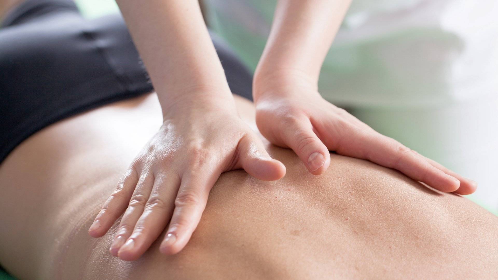 Hands of a massage therapist applying pressure to a client's back during a massage therapy session.