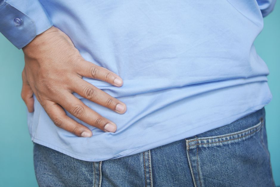 Person sitting on a sofa holding their lower back in discomfort